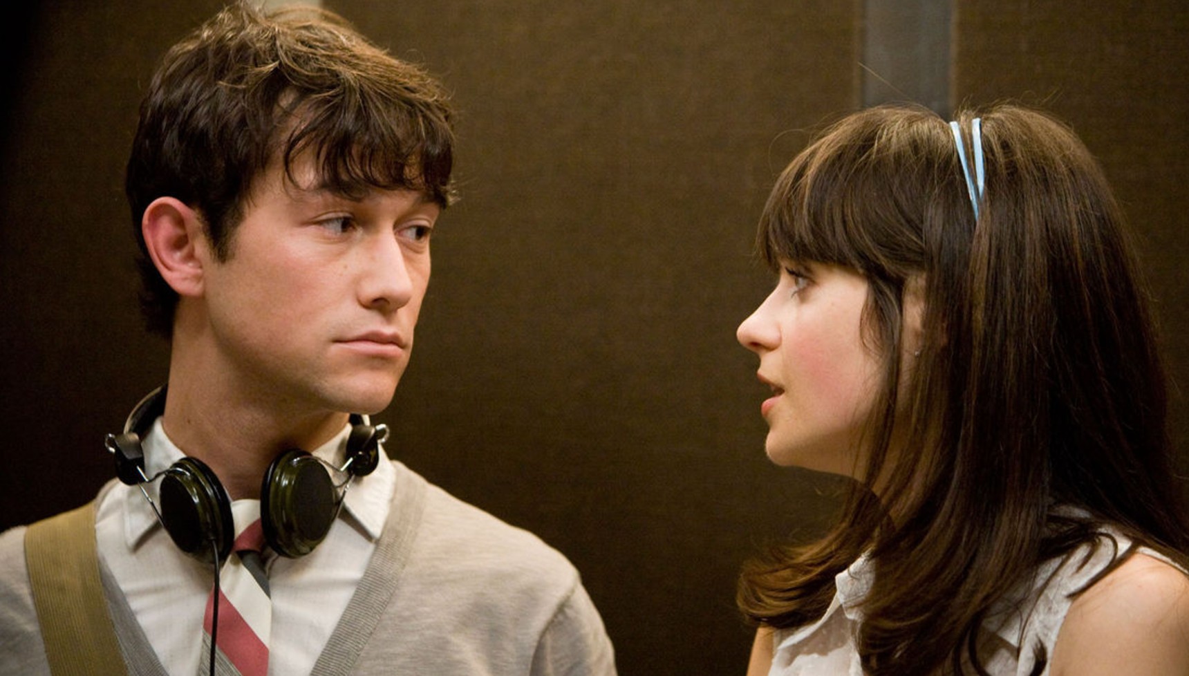 Joseph Gordon-Levitt with headphones around his neck as Zooey Deschanel talks to him in 500 Days of Summer