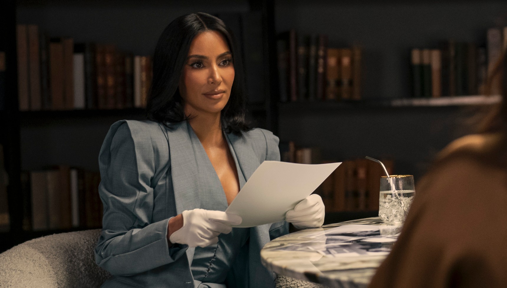Kim Kardashian wearing white gloves and holding a document in All's Fair