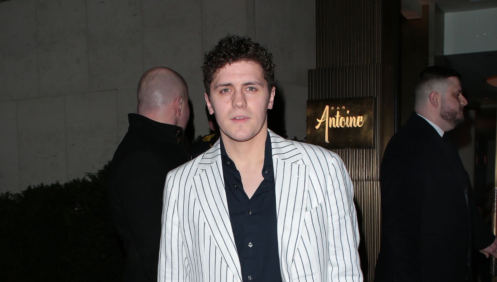 Dylan Llewellyn wears a black shirt and white and black striped blazer