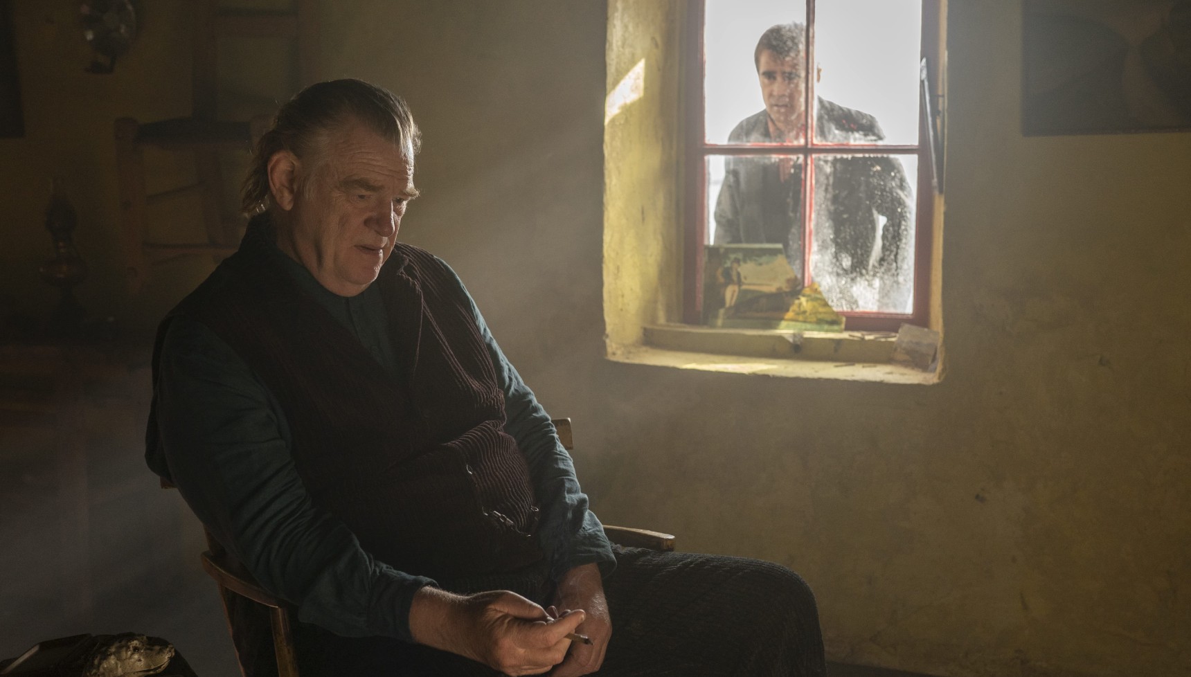 Colin Farrell looking through a window at Brendan Gleeson sitting alone