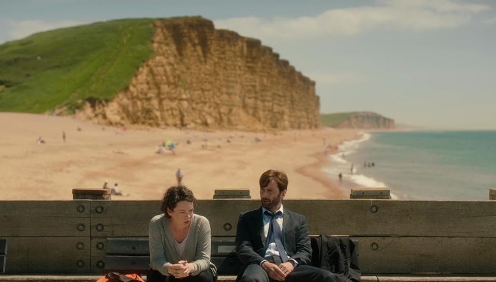 Olivia Colman and David Tennant sitting on a bench on the pier near the beach in Broadchurch