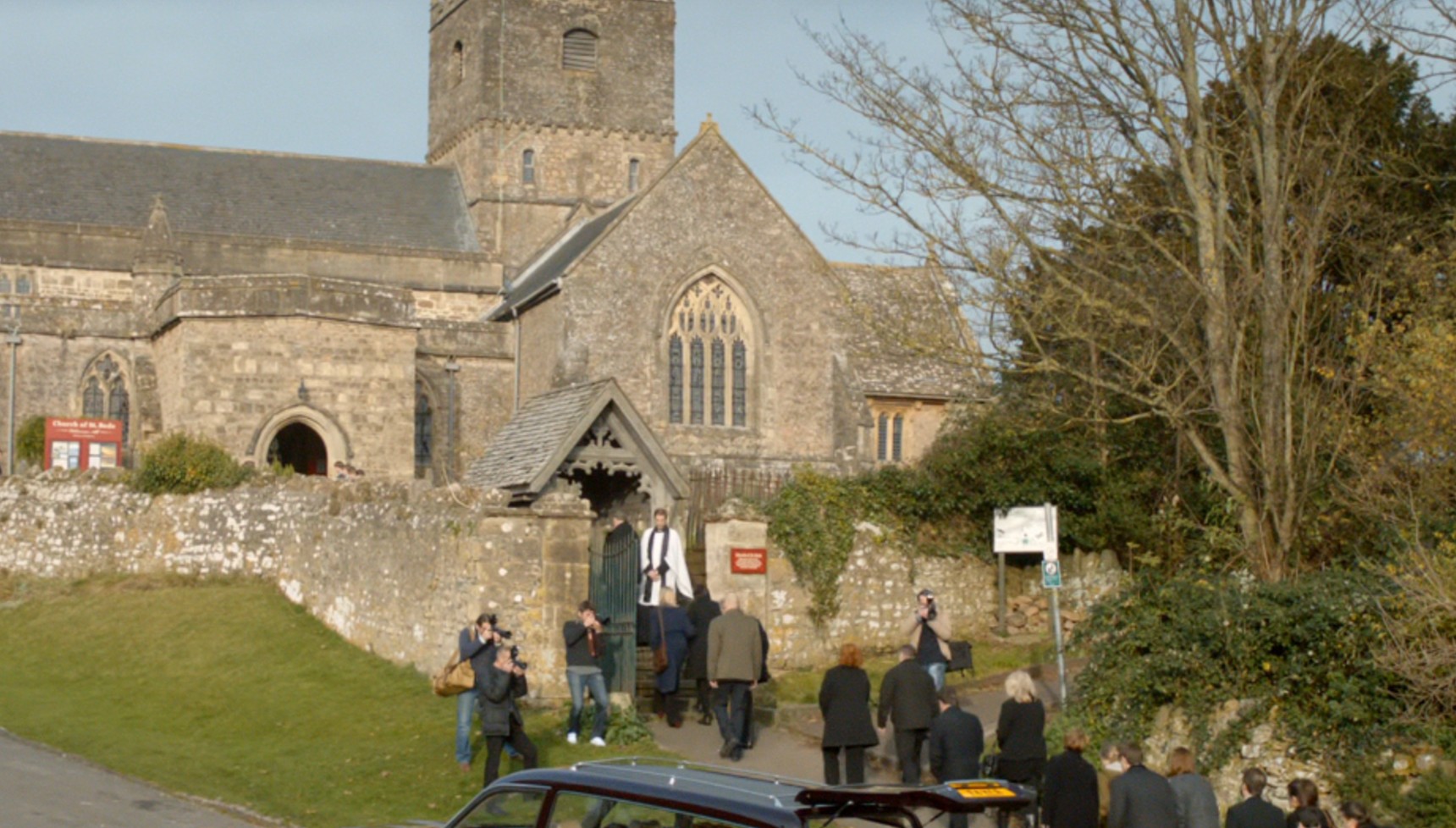 People in black and grey clothes walking into a church in Broadchurch