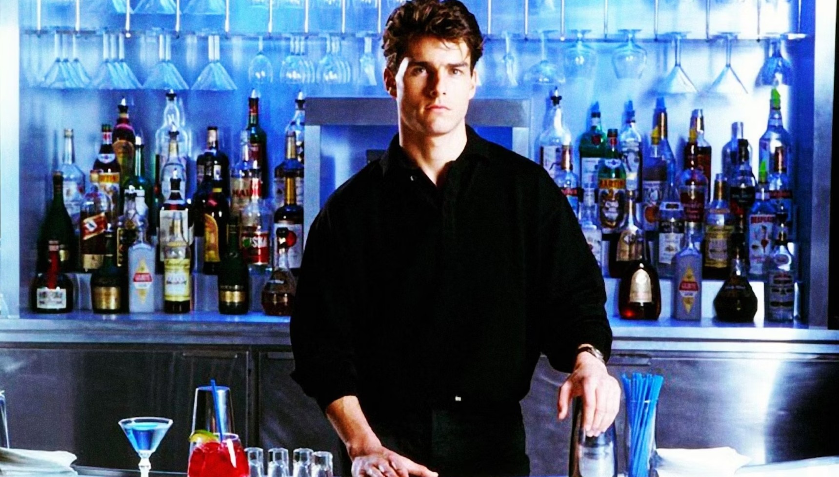 Tom Cruise standing in front of a bar in a black shirt in Cocktail