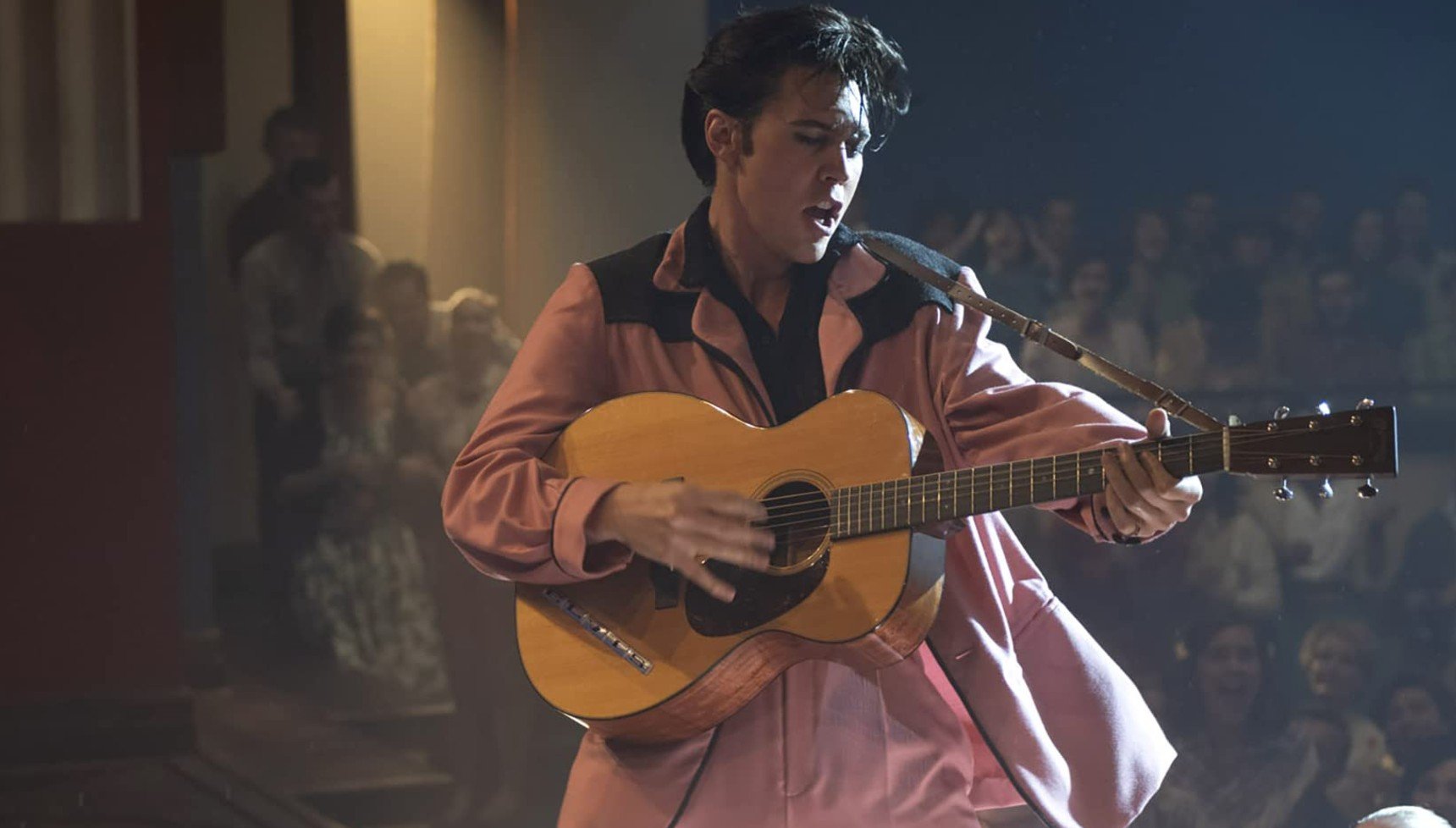 Austin Butler playing guitar in a pink suit in Elvis