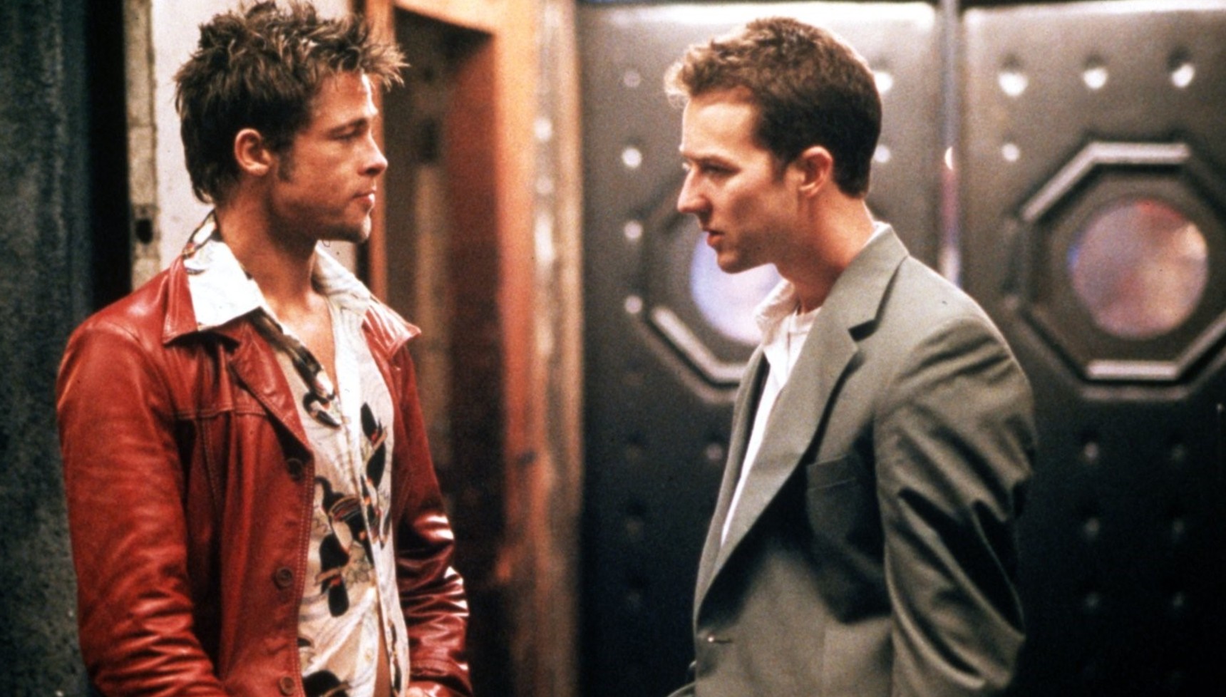 Edward Norton in a grey suit talking to Brad Pitt in a red leather coat in Fight Club
