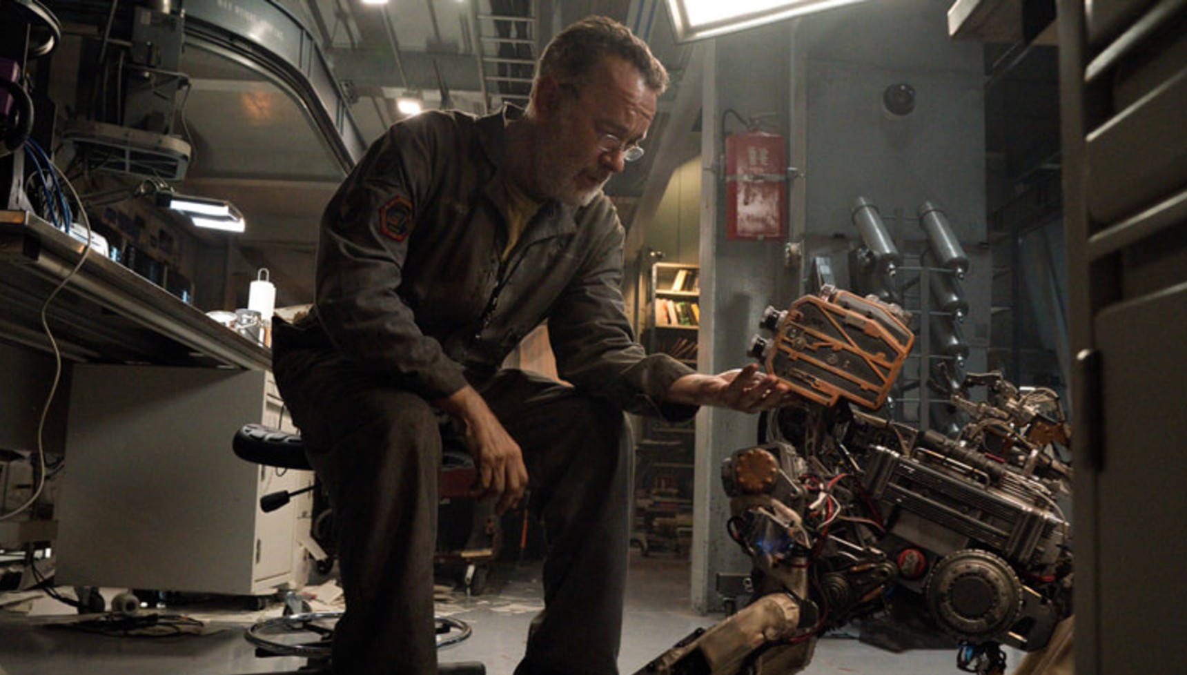 A bearded Tom Hanks tinkers with a robot