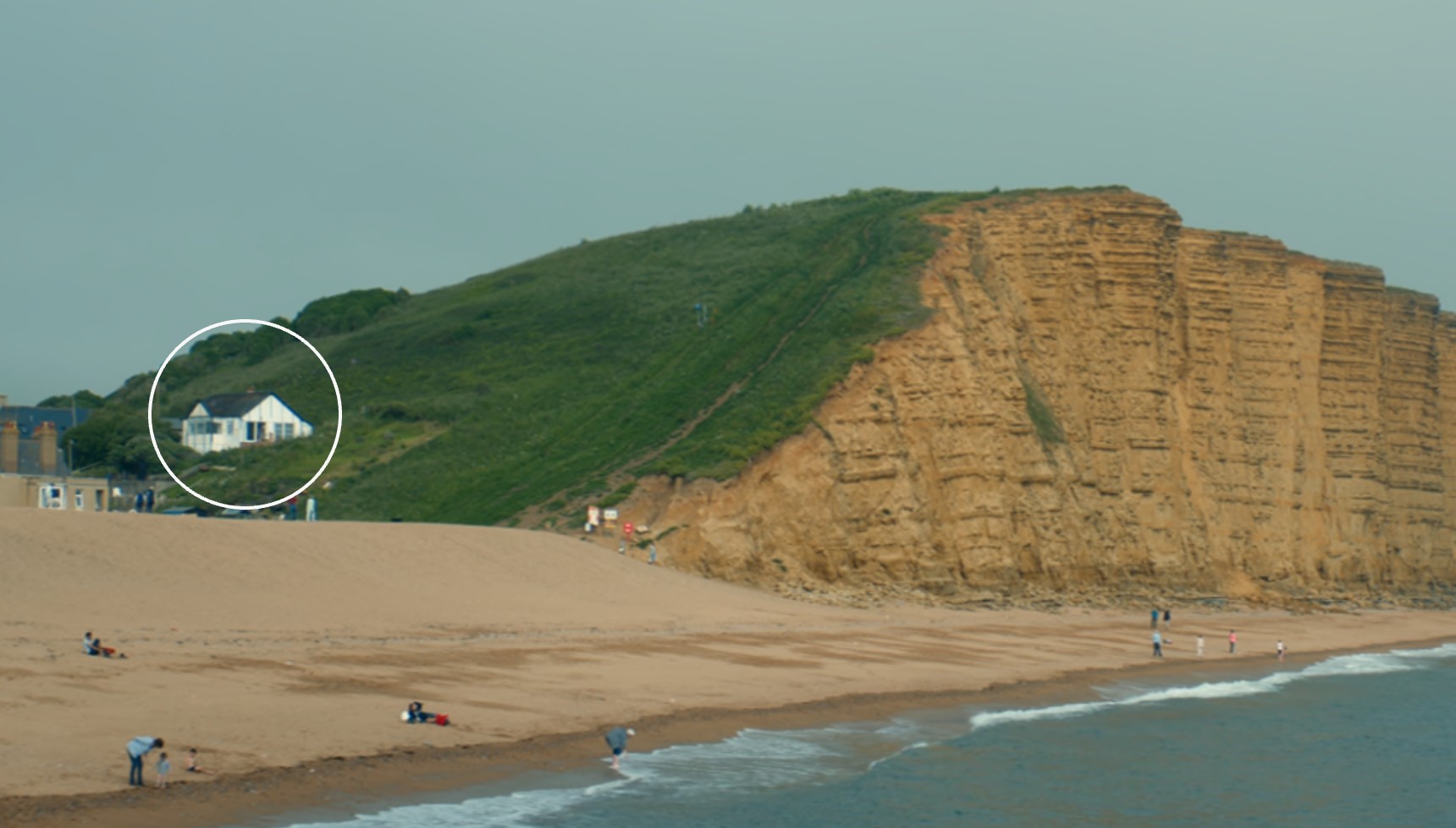 The Jurassic Coast cliff in Broadchurch with a small white house on its grass, with a white circle indicating where a reader should look