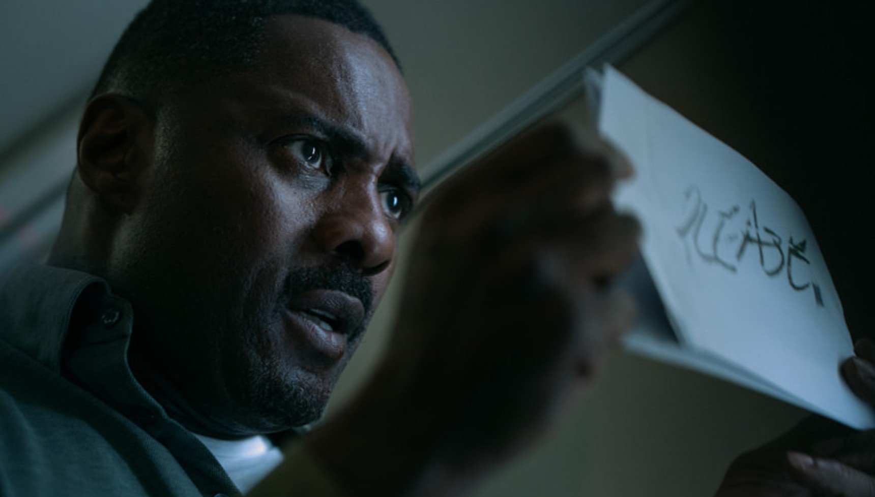 Man holding up a piece of paper that has 'PLEASE' scribbled on it