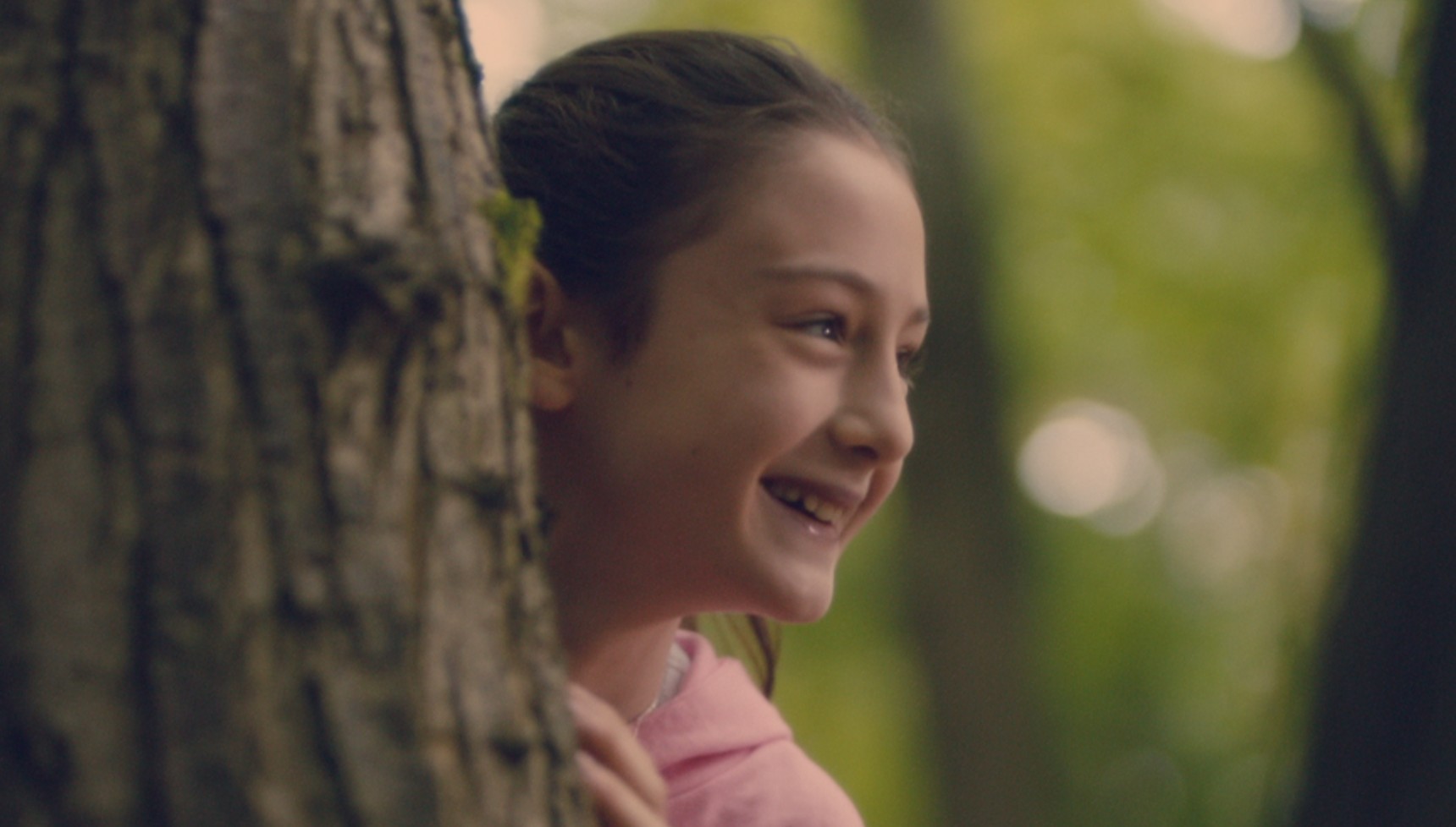 Hollie Burgess peaking from a tree and smiling in Broadchurch