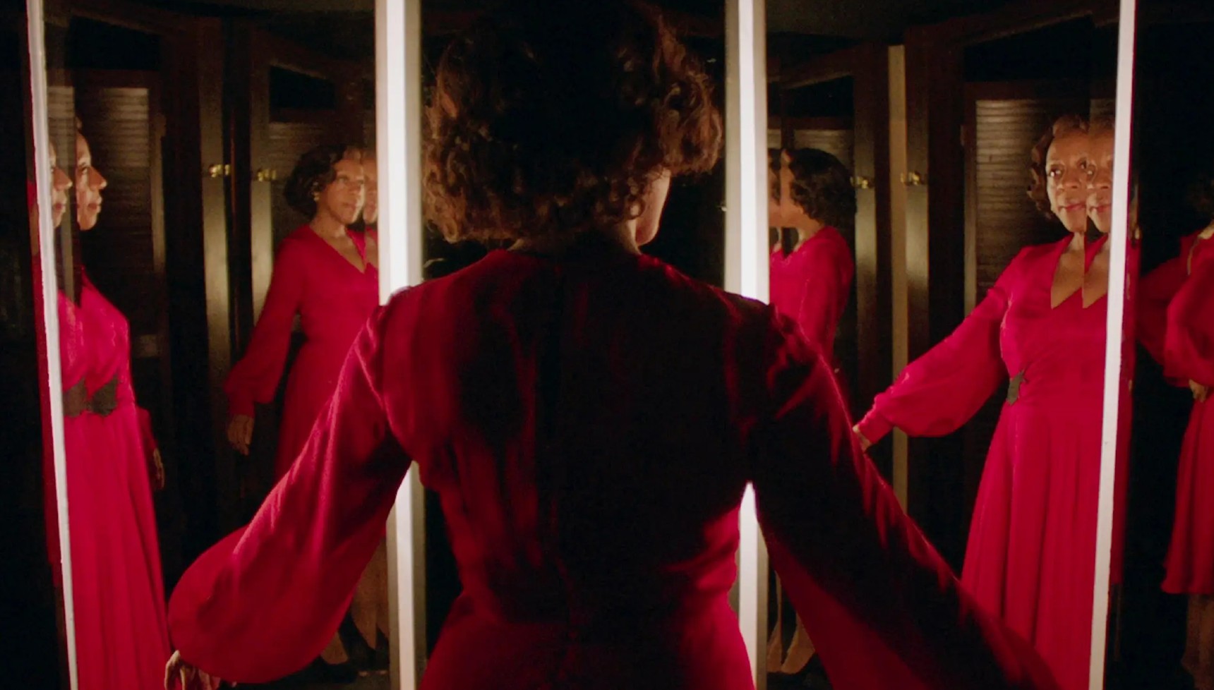 Marianne Jean-Baptiste looking at herself in multiple mirrors while wearing a red dress