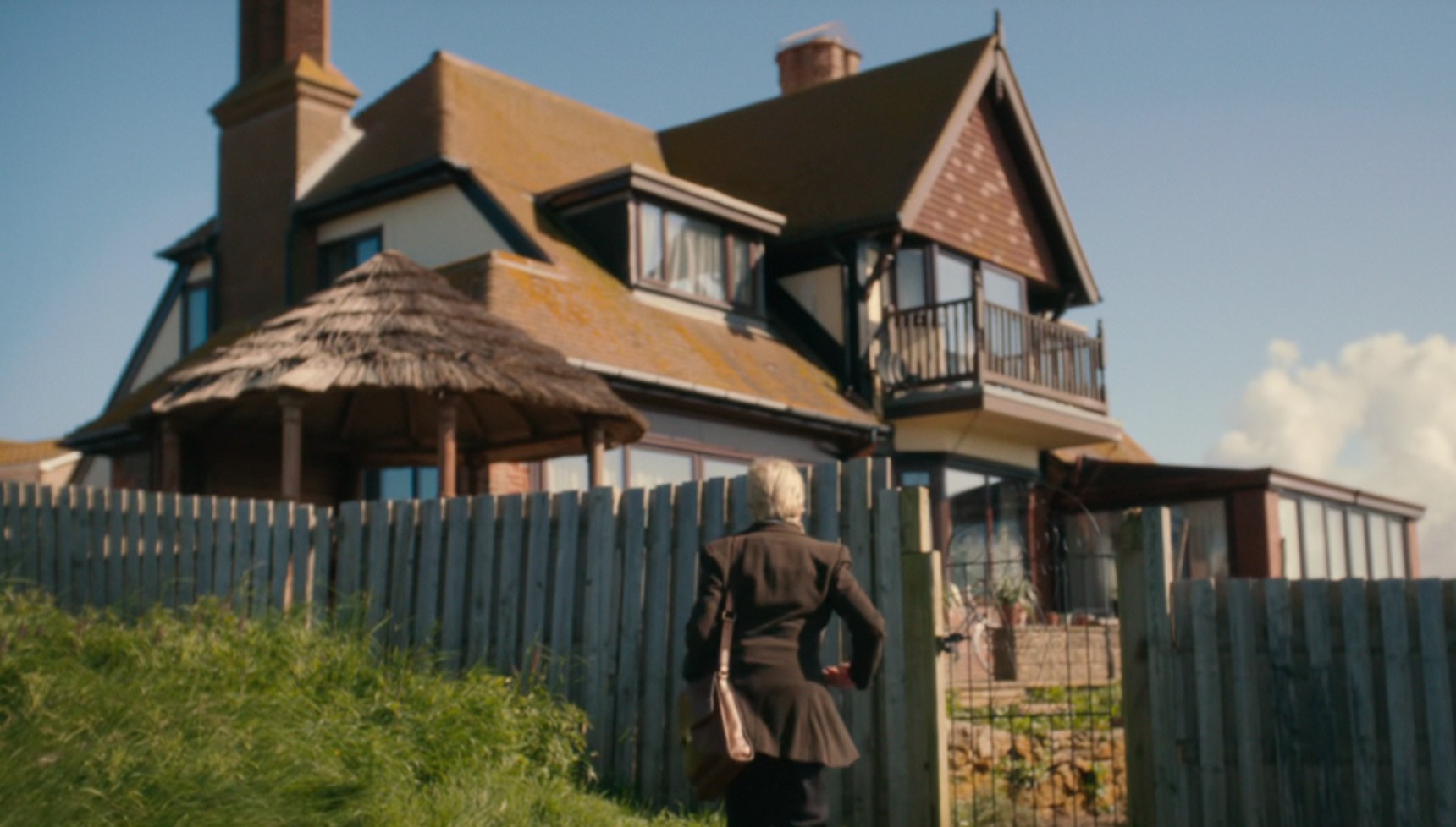 A woman walking towards a large brown and white house, where Broadchurch filmed its Jocelyn Knight house scenes