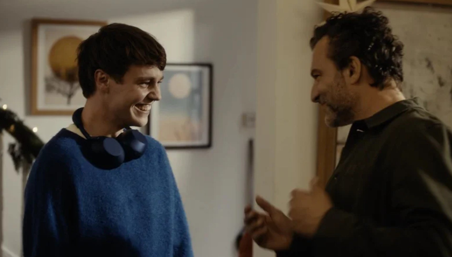 A teenager in a blue jumper wearing headphones next to his dad as he dances in the John Lewis Christmas ad