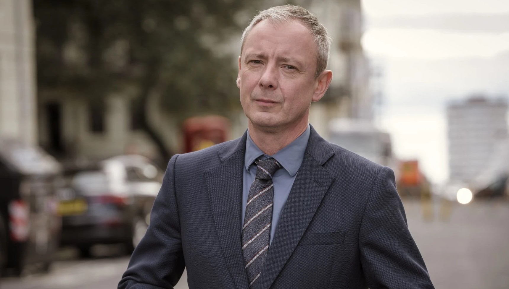 Jon Simm in a grey and blue suit in Grace