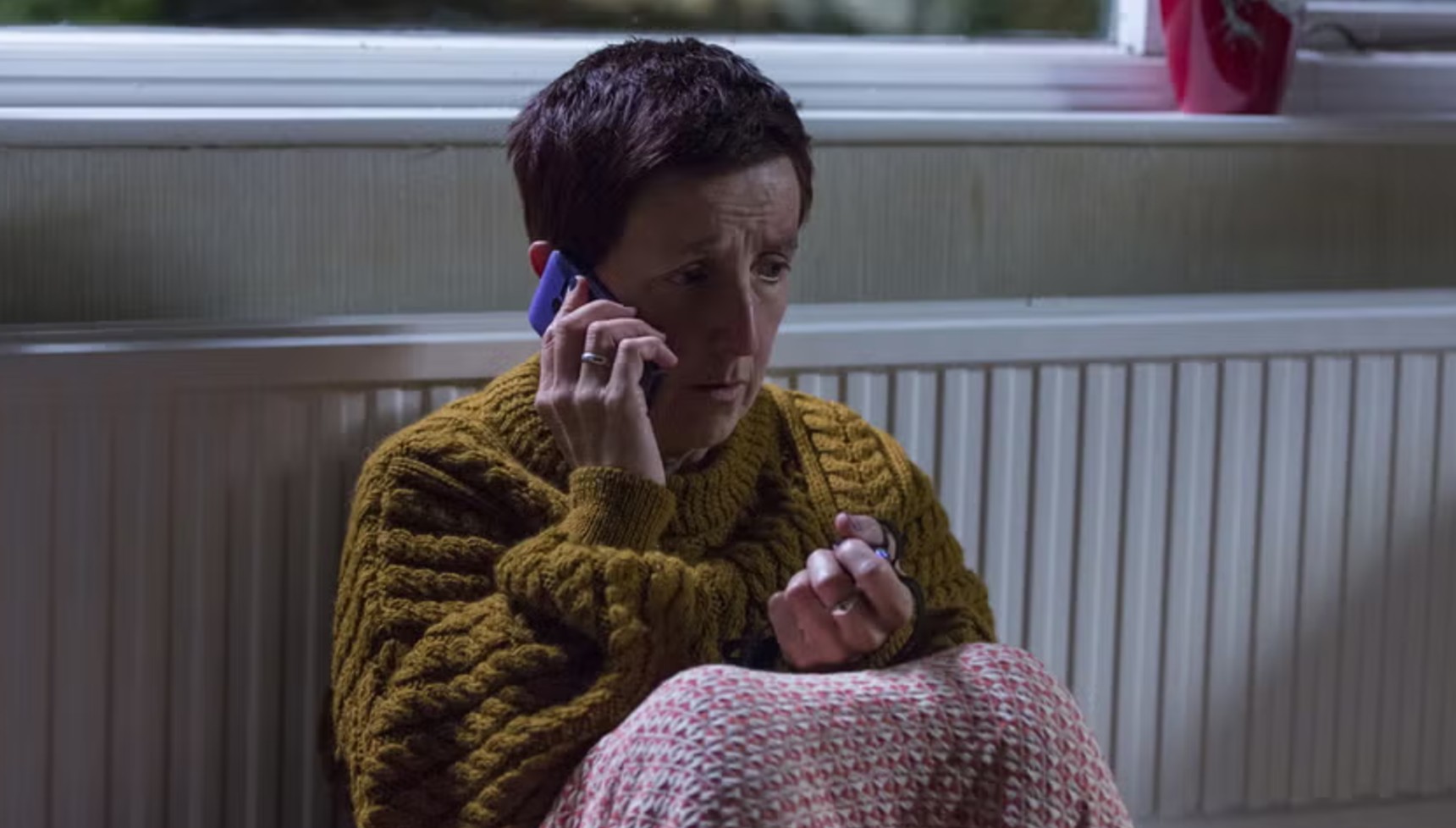 Julie Hesmondhalgh sitting against a radiator on the phone in Broadchurch