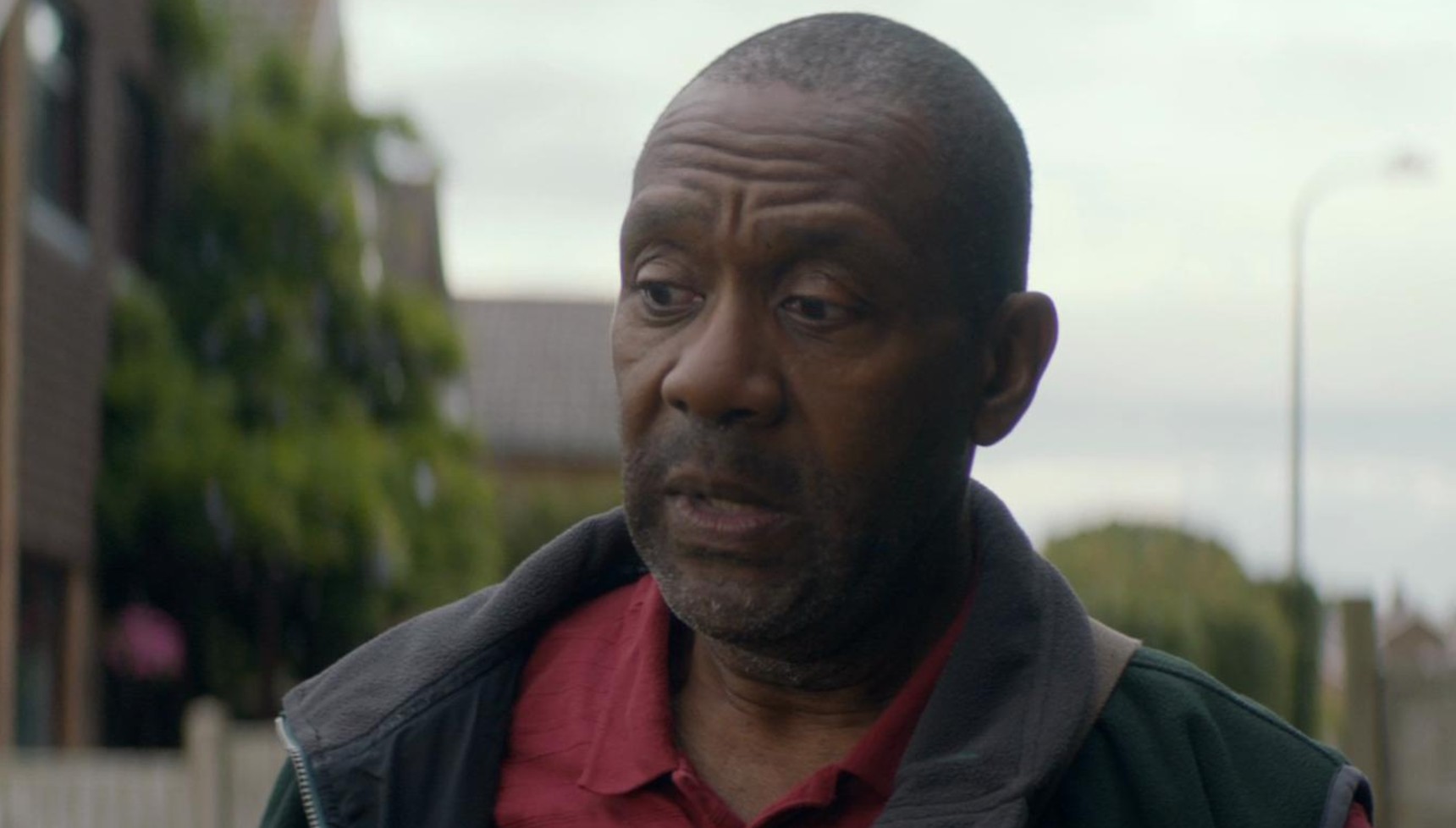 Lenny Henry in a red shirt and dark grey body warmer in Broadchurch