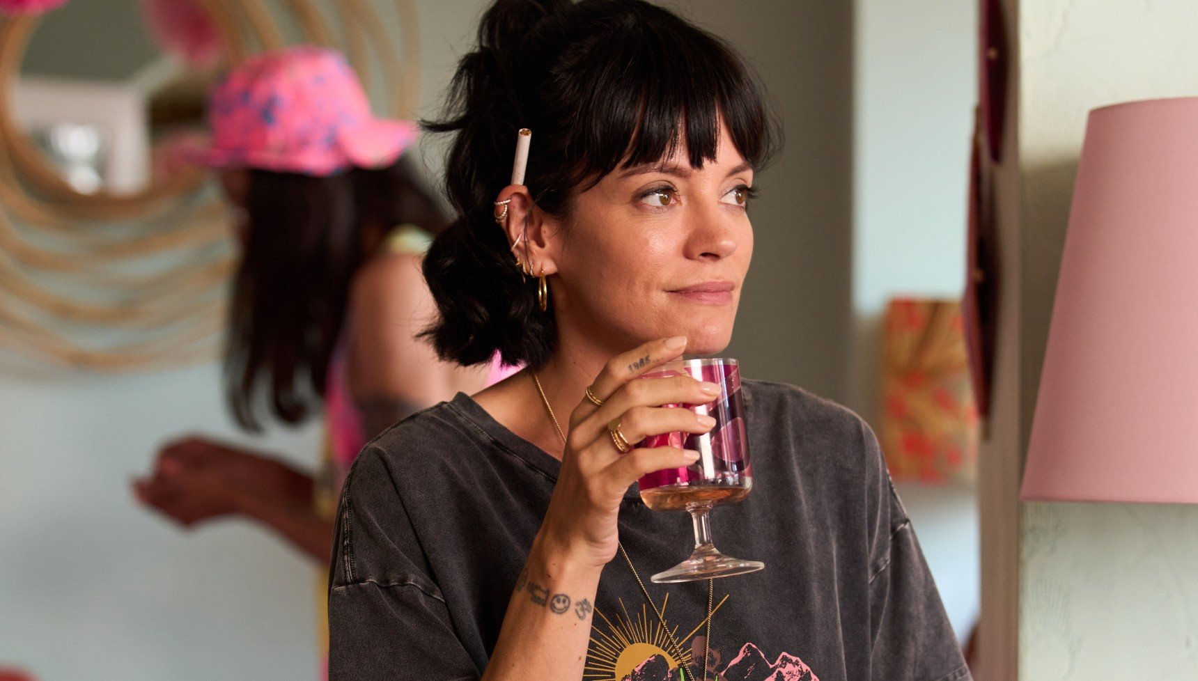 Lily Allen holding a glass with a cigarette behind her ear in Dreamland