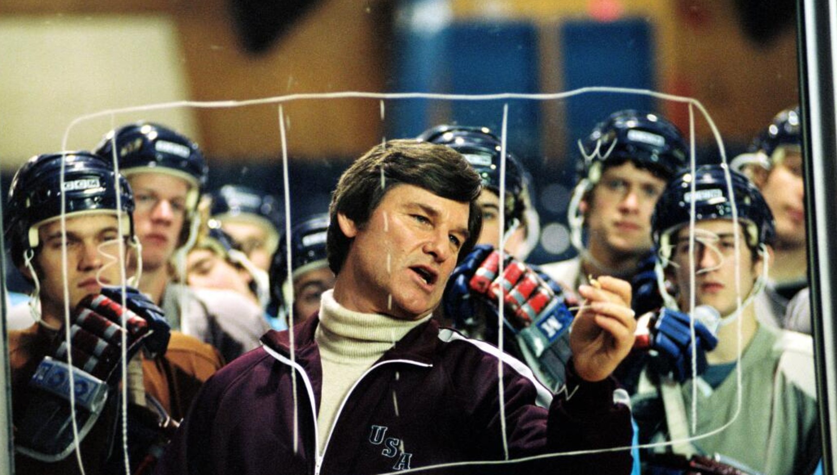 Kurt Russell in costume as Herb Brooks instructing his hockey team on a play in Miracle