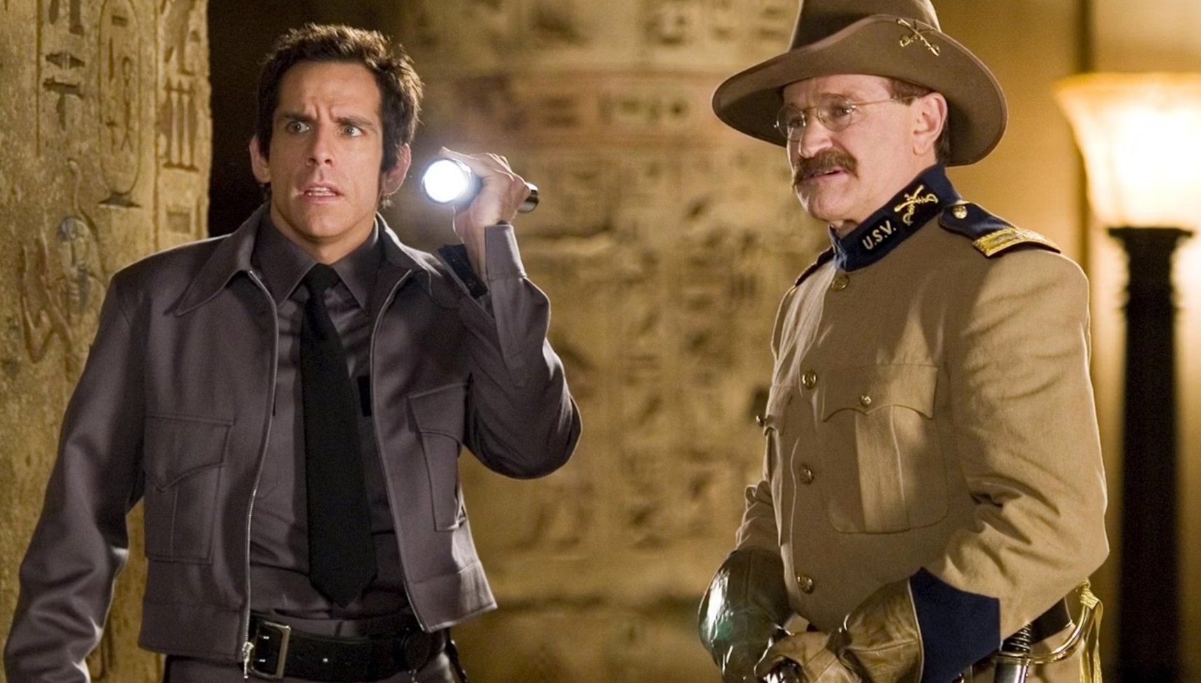 Ben Stiller in a night watchman outfit holding a flashlight next to Robin Williams in costume as Theodore Roosevelt in Night at the Museum