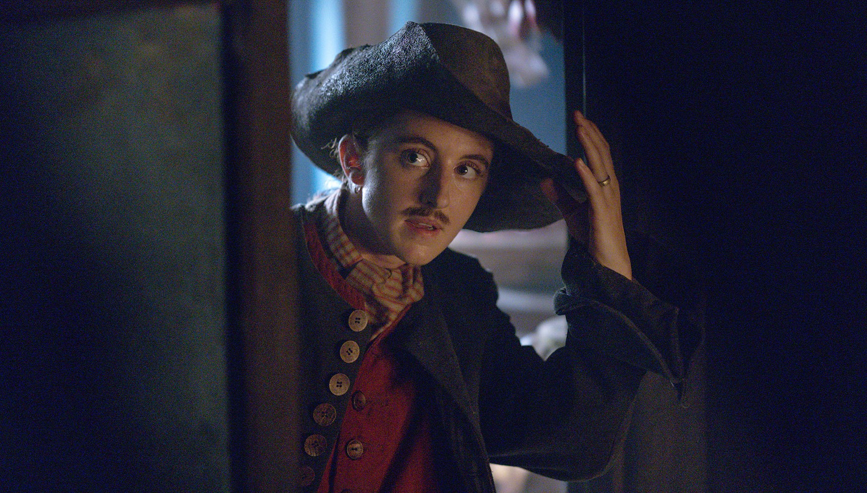 Louisa Harland's Renegade Nell touches her hat while peering into a room