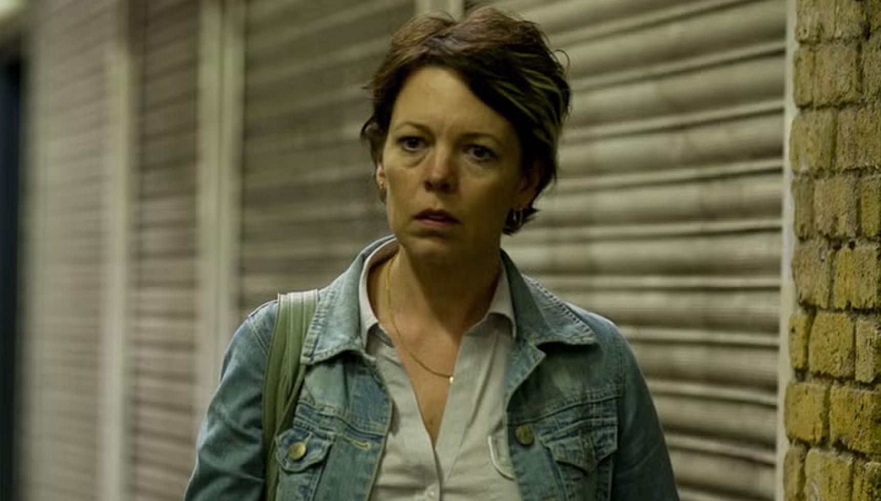 Olivia Colman wearing a denim jacket and standing in front of a shutter in Run