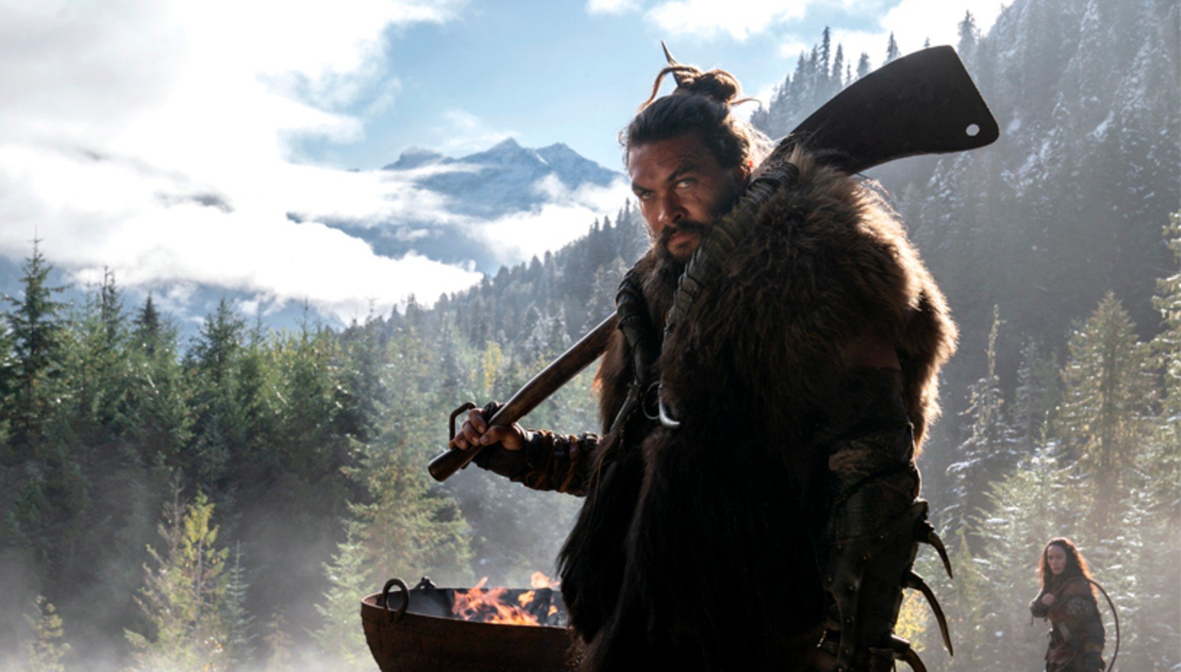 A tribesman holding a weapon with mountains in the background