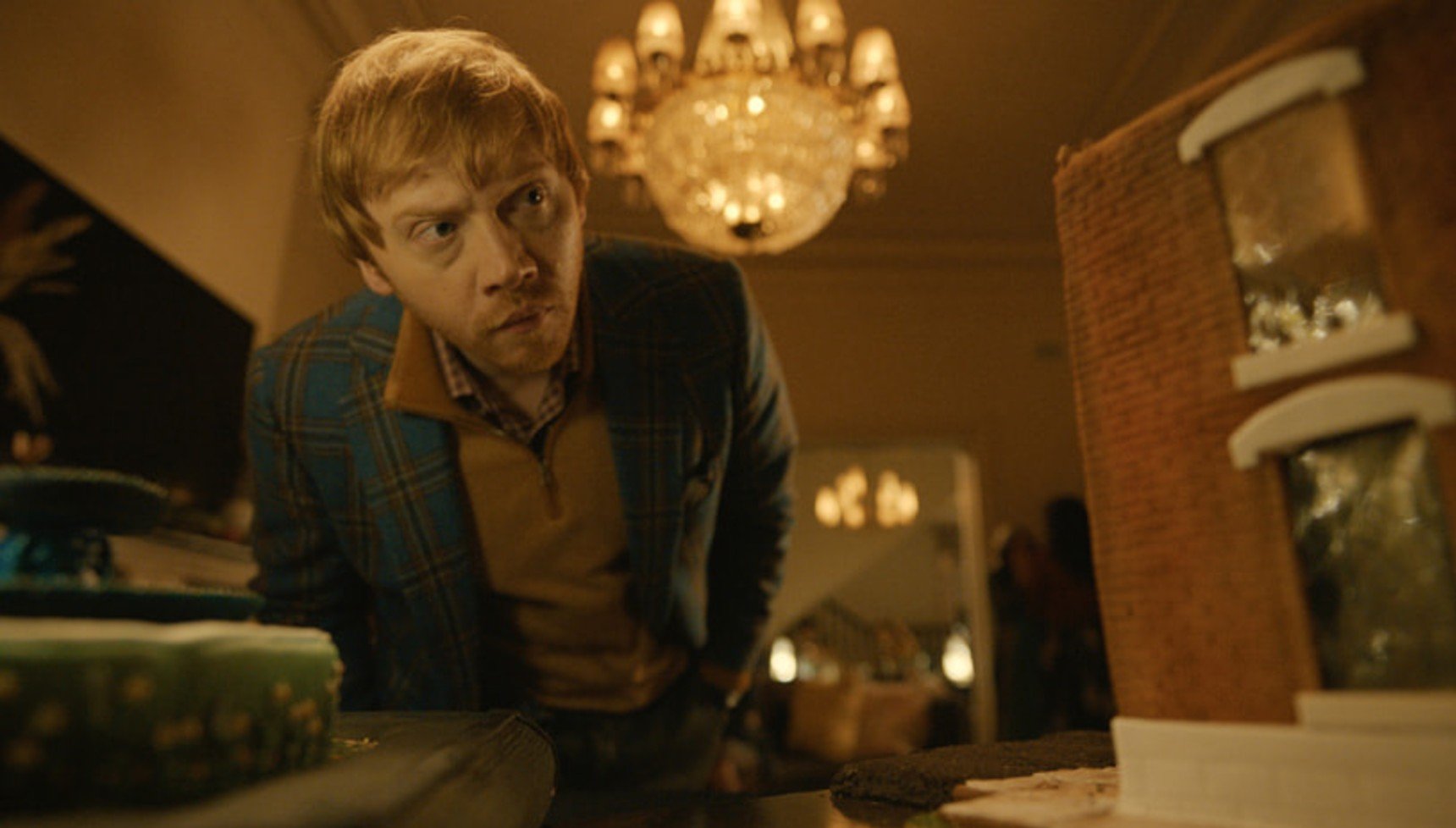 Red-haired man peers at a model house in Servant