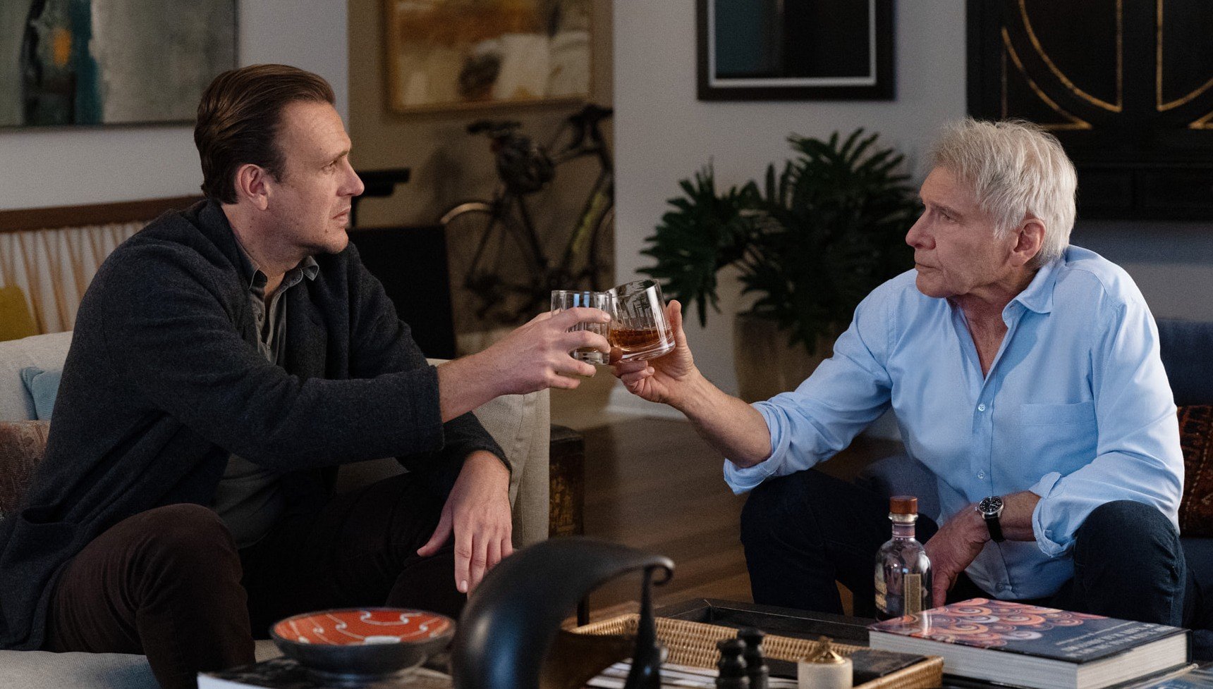 Two men sitting down clinking their glasses together