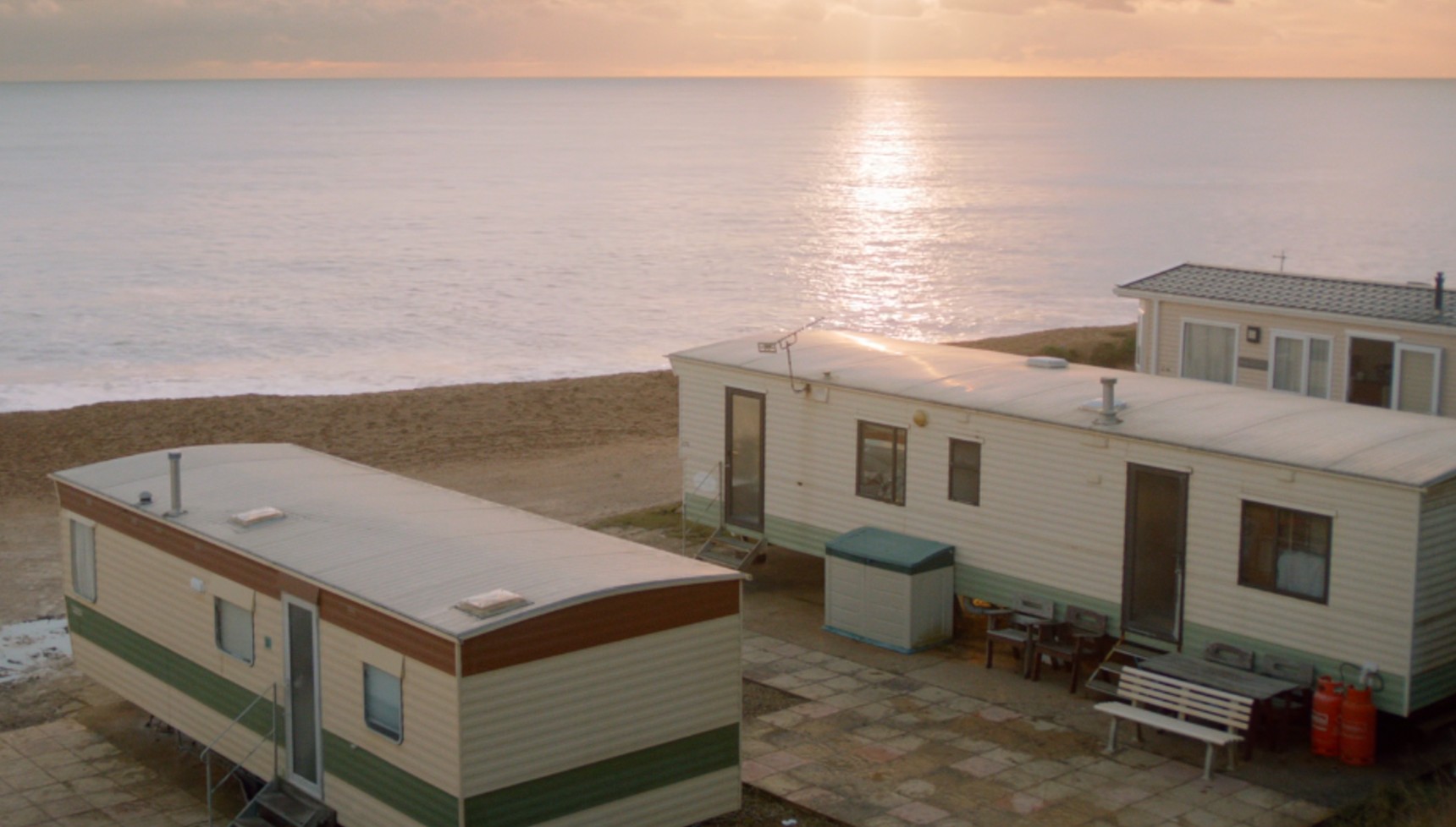 Two caravans on a beach as the sun reflects on the sea in Broadchurch