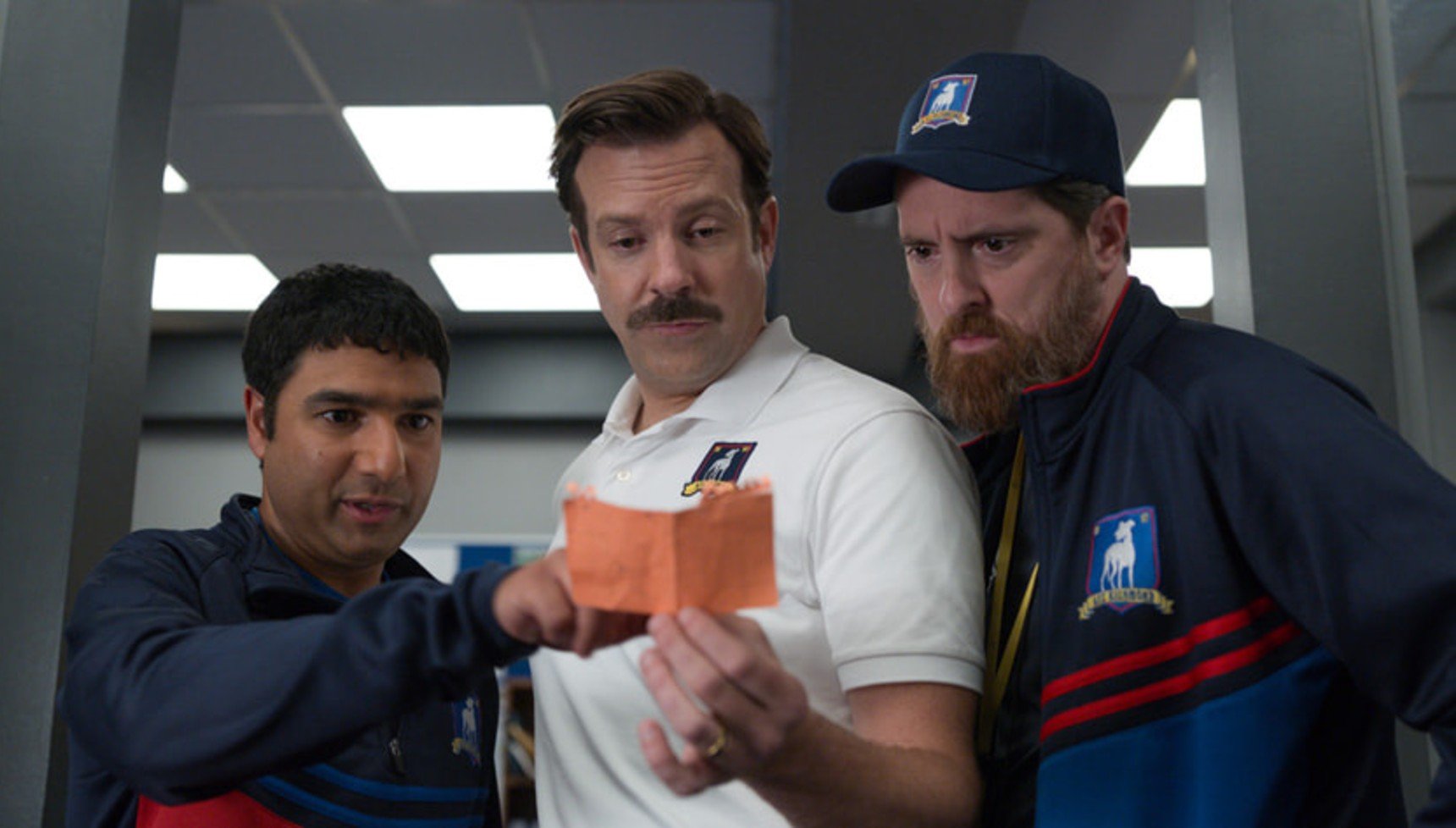 Three football coaches look at a piece of paper in Ted Lasso