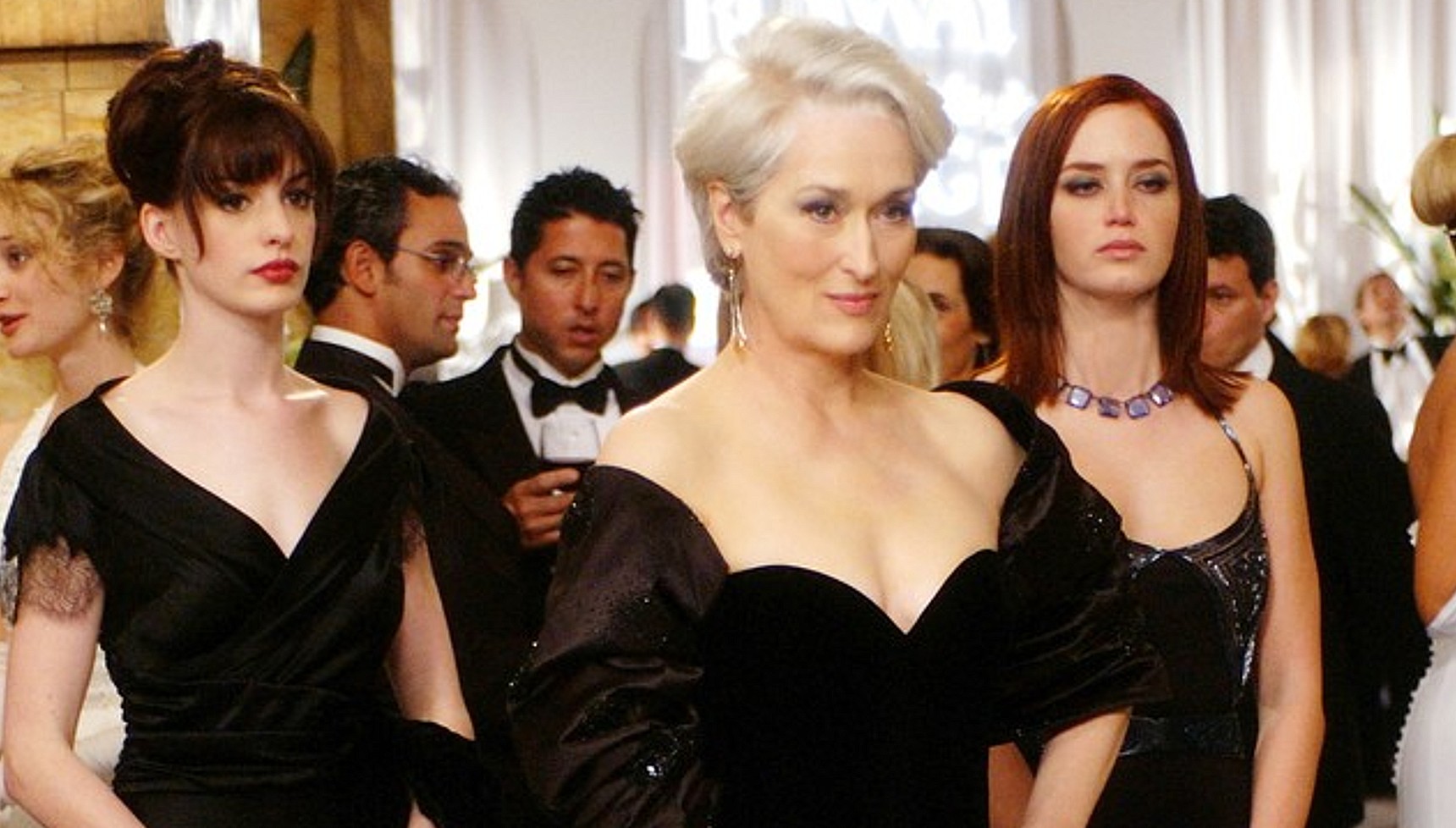 Anne Hathaway, Meryl Streep, and Emily Blunt wearing black dresses next to each other in The Devil Wears Prada