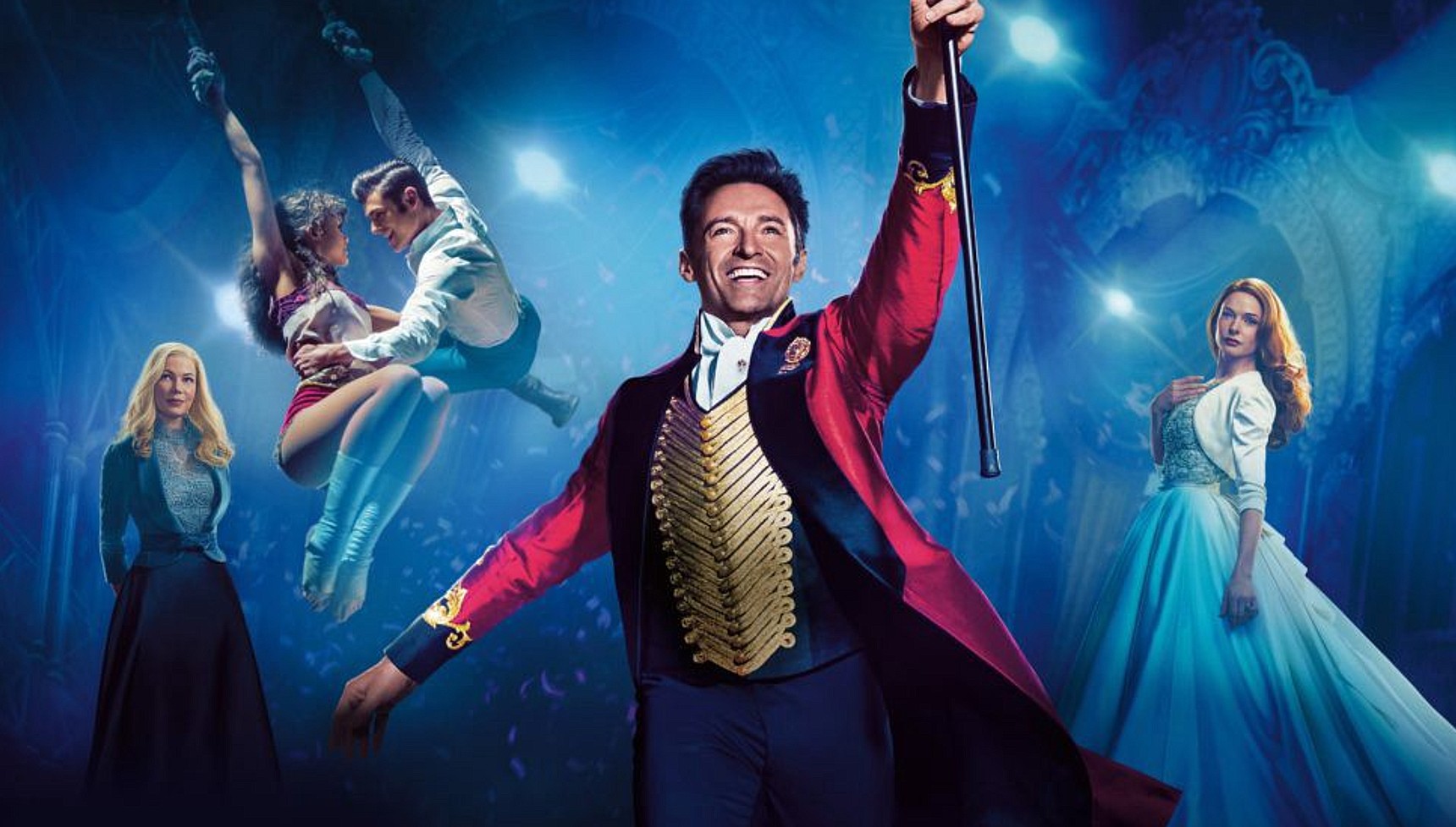 Hugh Jackman in a red jacket holding a cane with other cast members in The Greatest Showman behind him