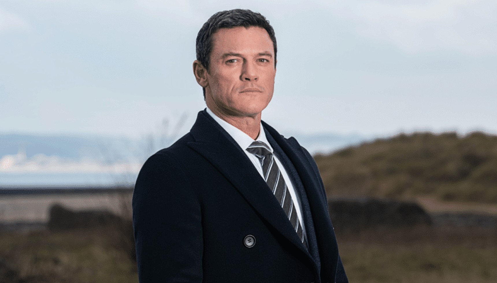 Luke Evans wearing a black jacket, shirt and tie in The Pembrokeshire Murders