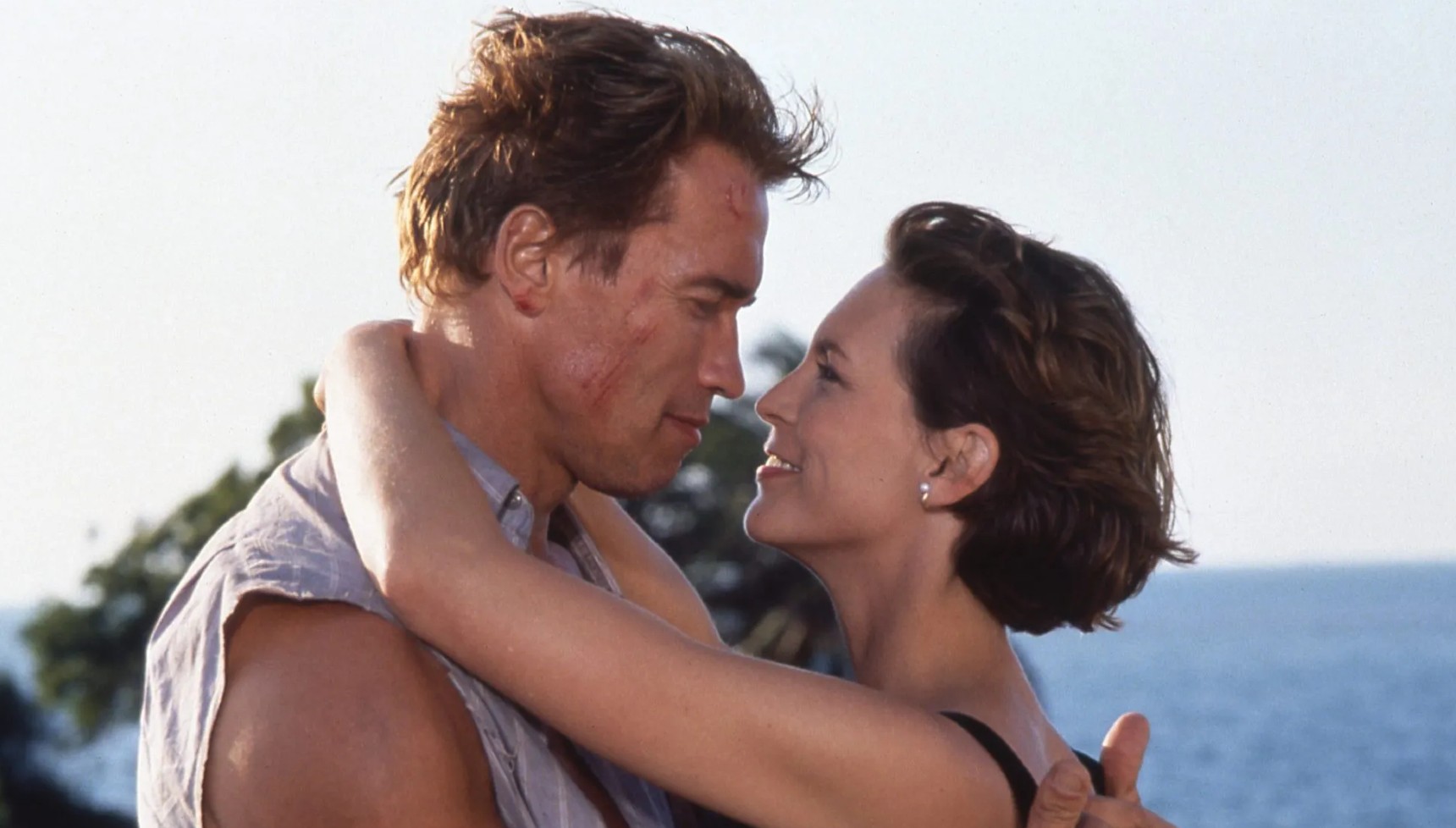Jamie Lee Curtis with her arms around Arnold Schwarzenegger's shoulders in True Lies