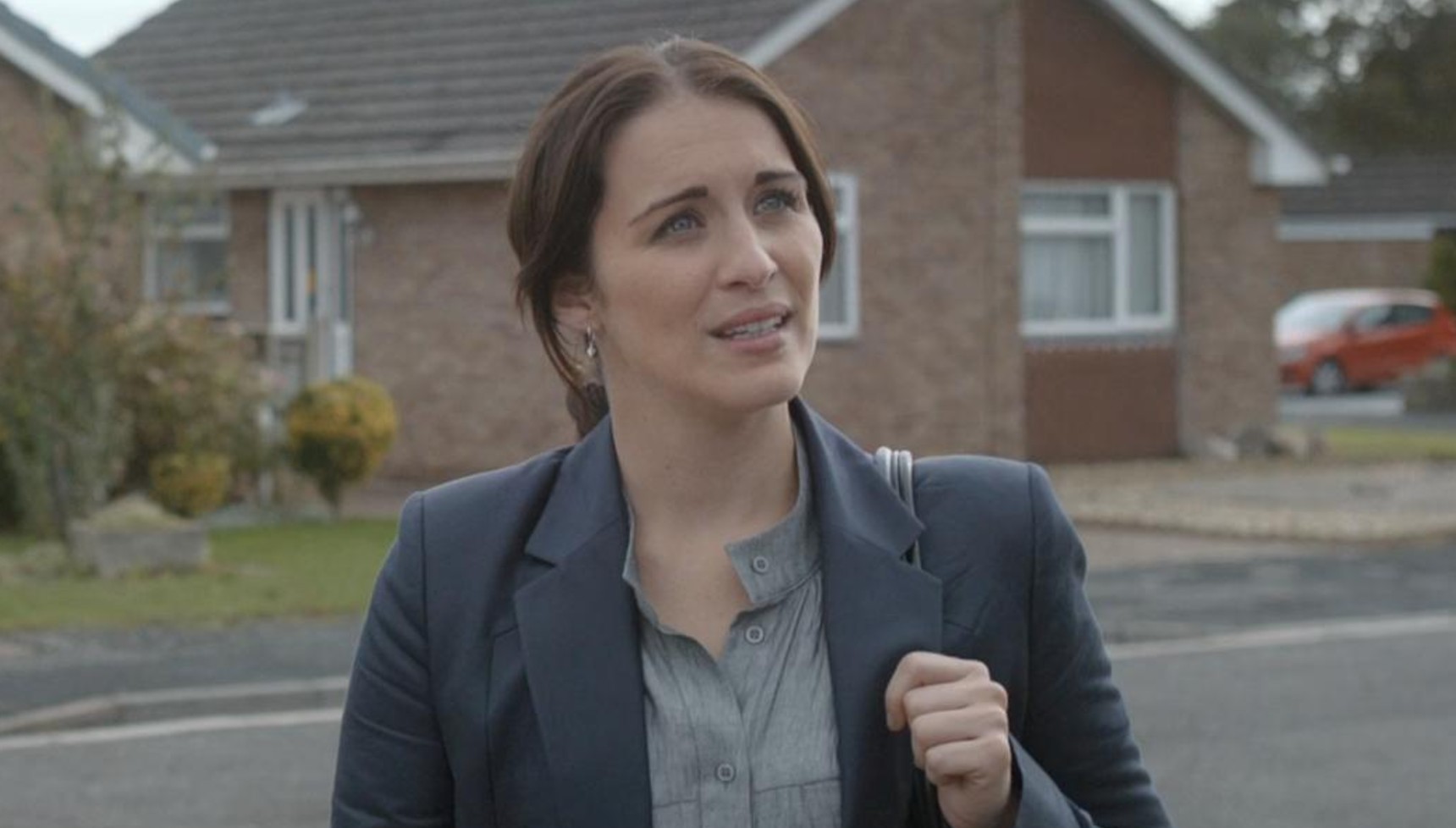 vicky McClure wearing a navy suit and standing on a residential street in Broadchurch