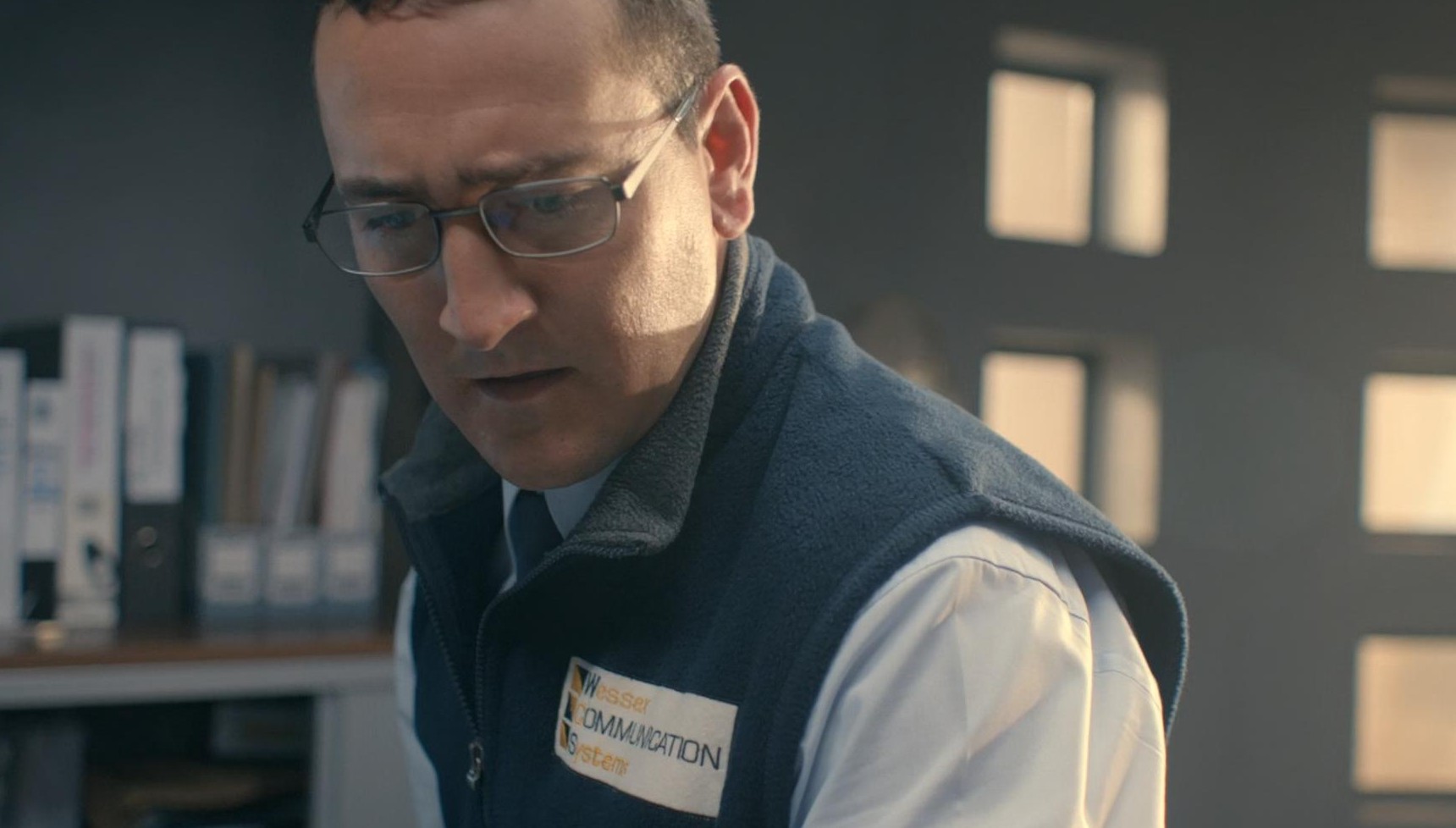 Will Mellor wearing a navy vest and glasses in Broadchurch