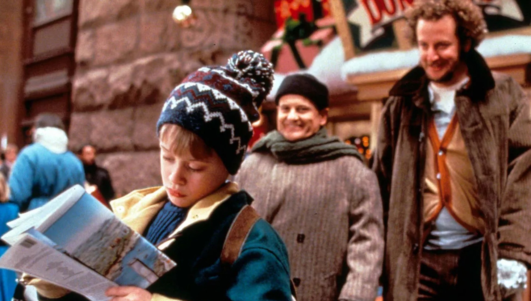 Macaulay Culkin looking at a map as Joe Pesci and Daniel Stern stand behind him in Home Alone 2