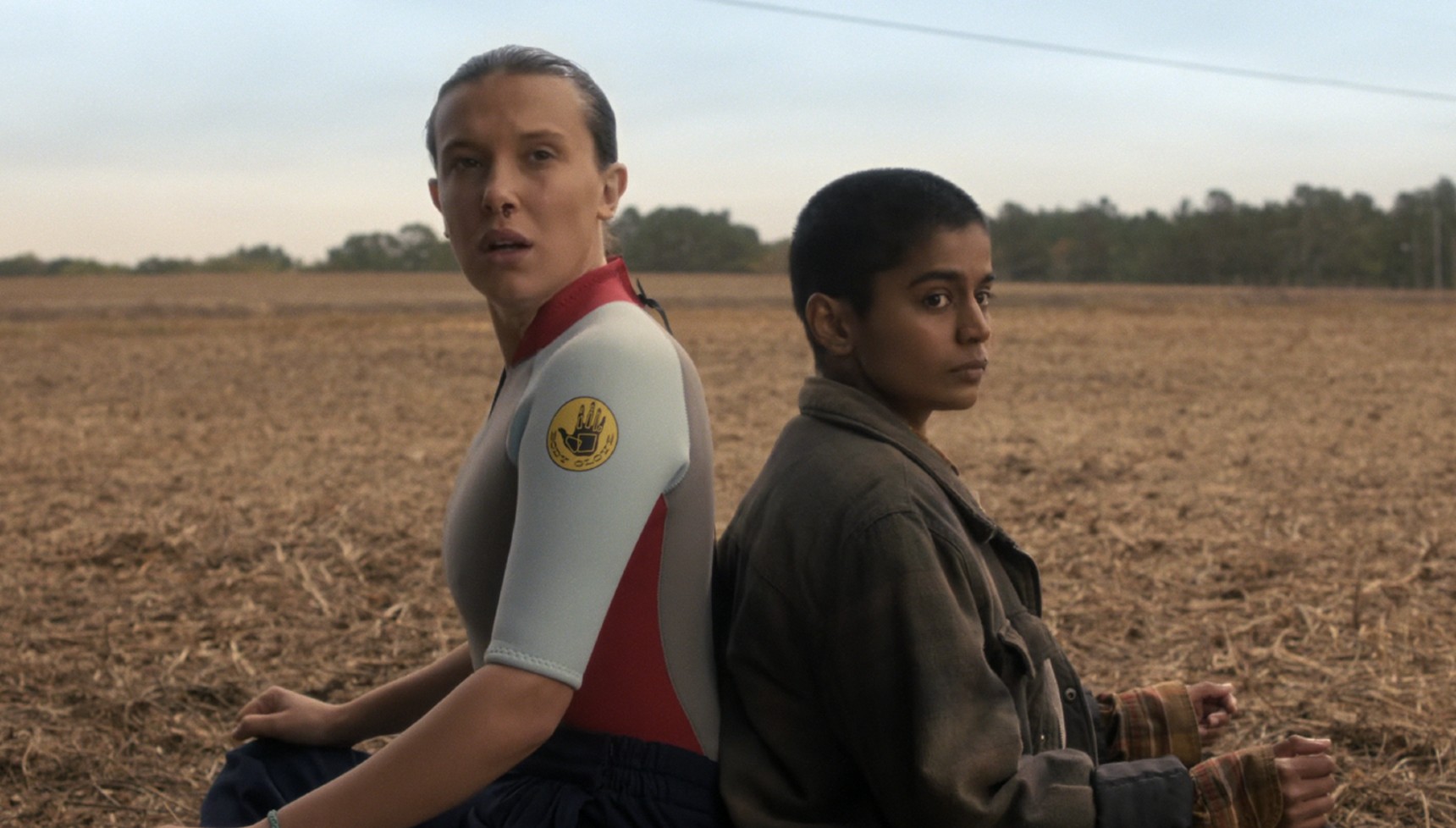 Eleven and Kali sitting back to back in a field in Stranger Things season 5 volume 2