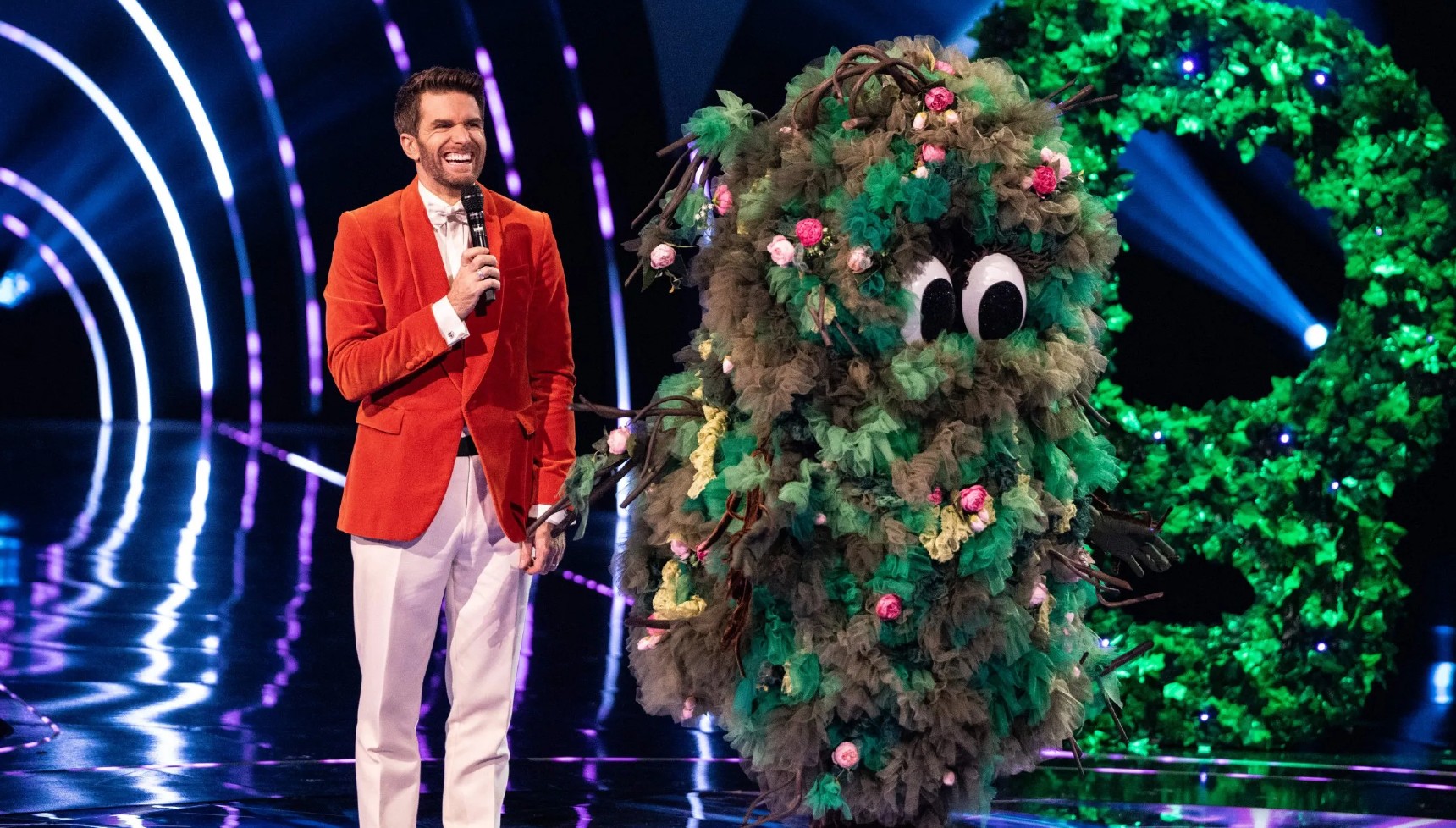 Joel Dommett standing next to a singer dressed as a bush on The Masked Singer
