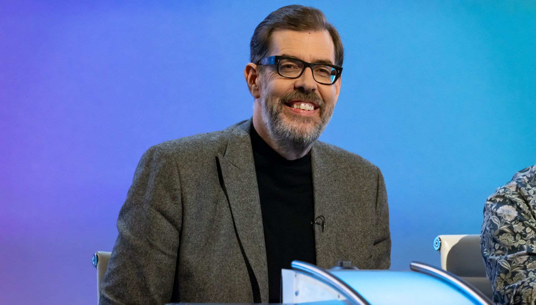 Richard Osman smilin against a blue background