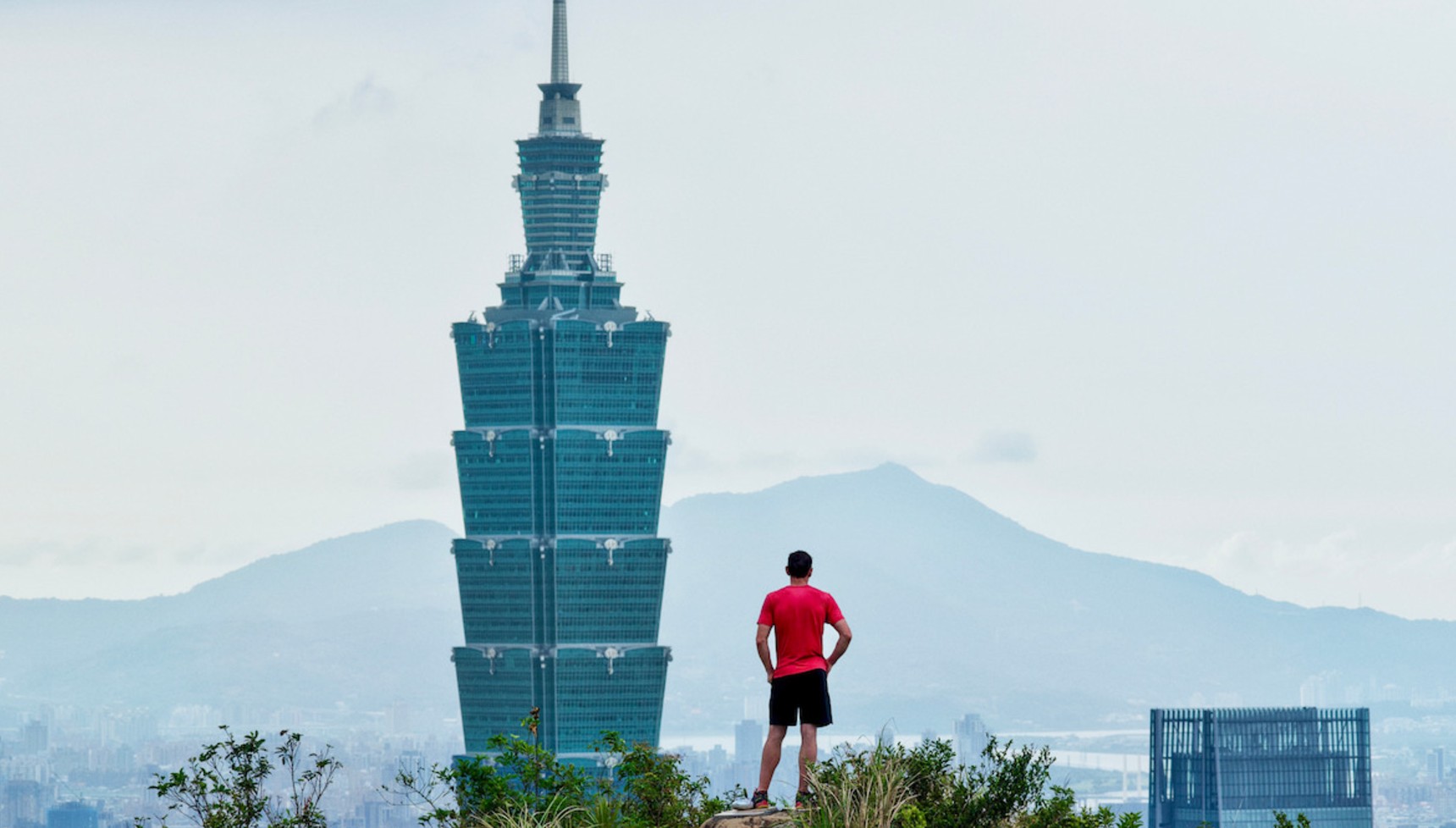 Alex Honnold standing on a hill looking at Taipei 101 