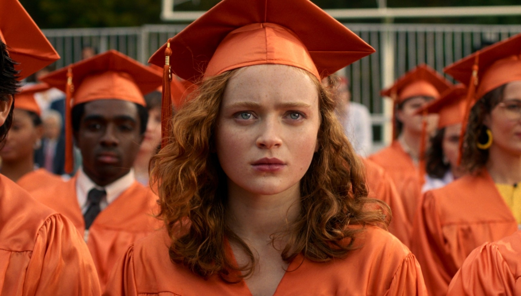 Max wearing an orange graduation gown in Stranger Things 