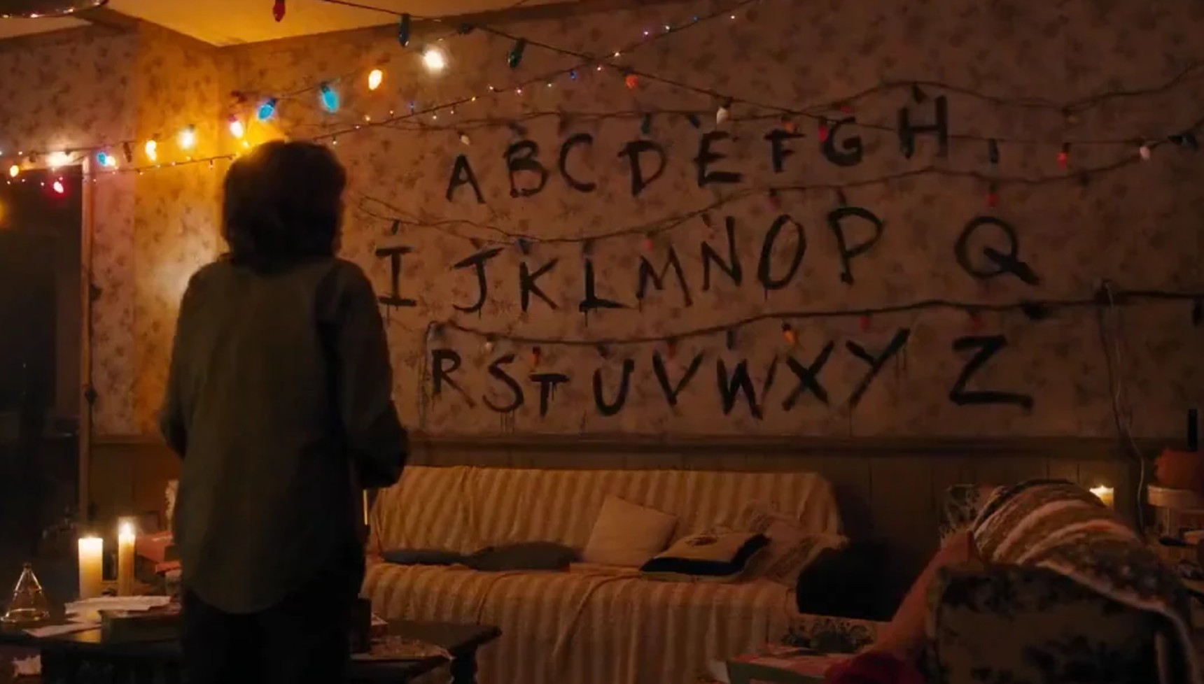 Joyce standing in front of letters on her wall with Christmas lights in Stranger Things season 1