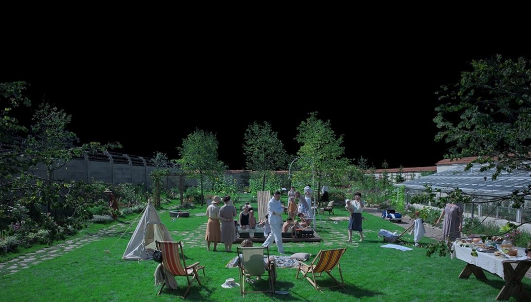 A family in a garden with a pitch black sky, the poster for The Zone of Interest