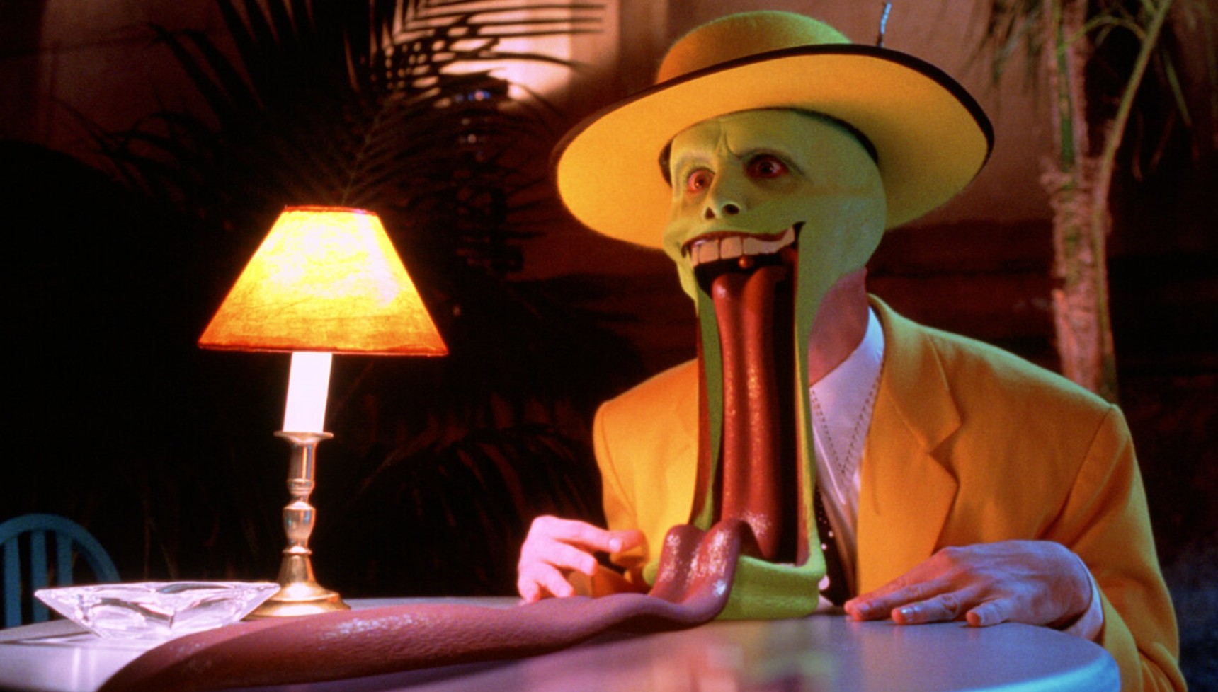 Jim Carrey in costume in The Mask with his tongue on the table