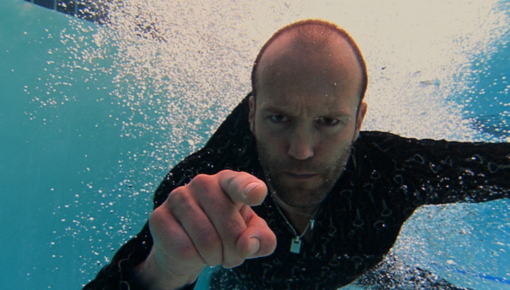 Jason Statham in a swimming pool pointing at the camera 