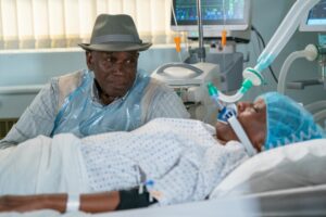 Patrick sits by Denise's hospital bed